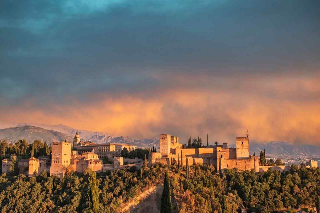 Panoramic view of the Alhambra in Granada, Spain, during sunset with the Sierra Nevada mountains in the background.