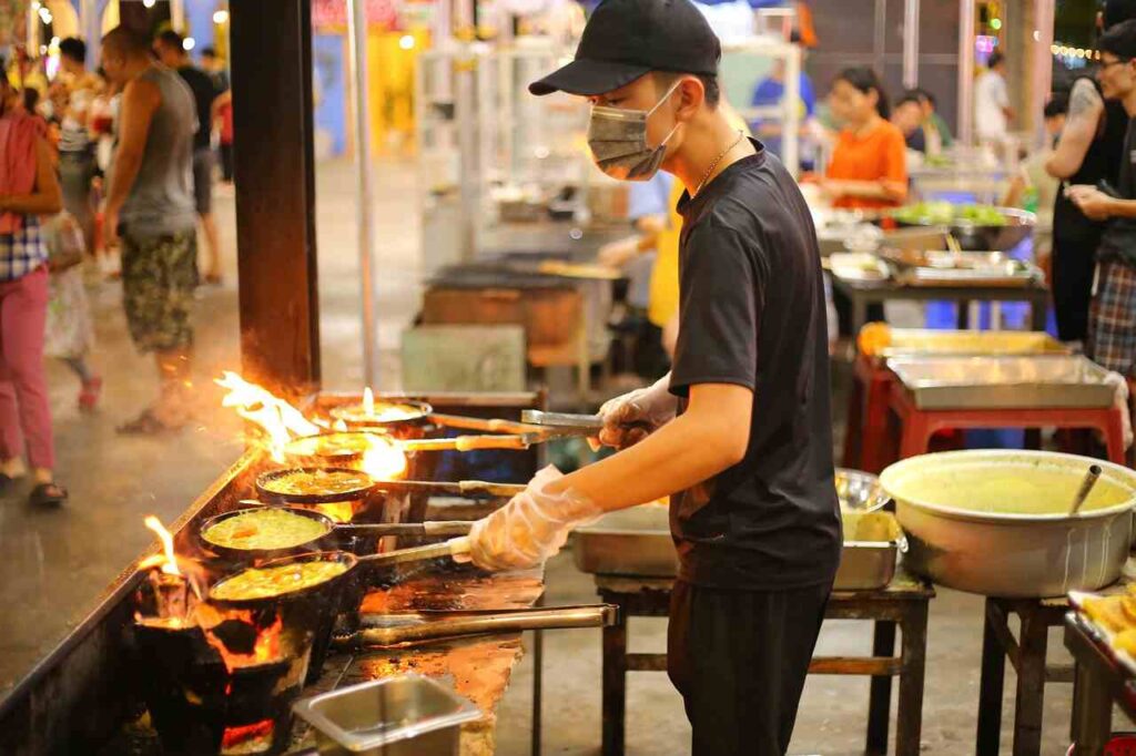 a man cooking food in a kitchen best for Traveling On Budget