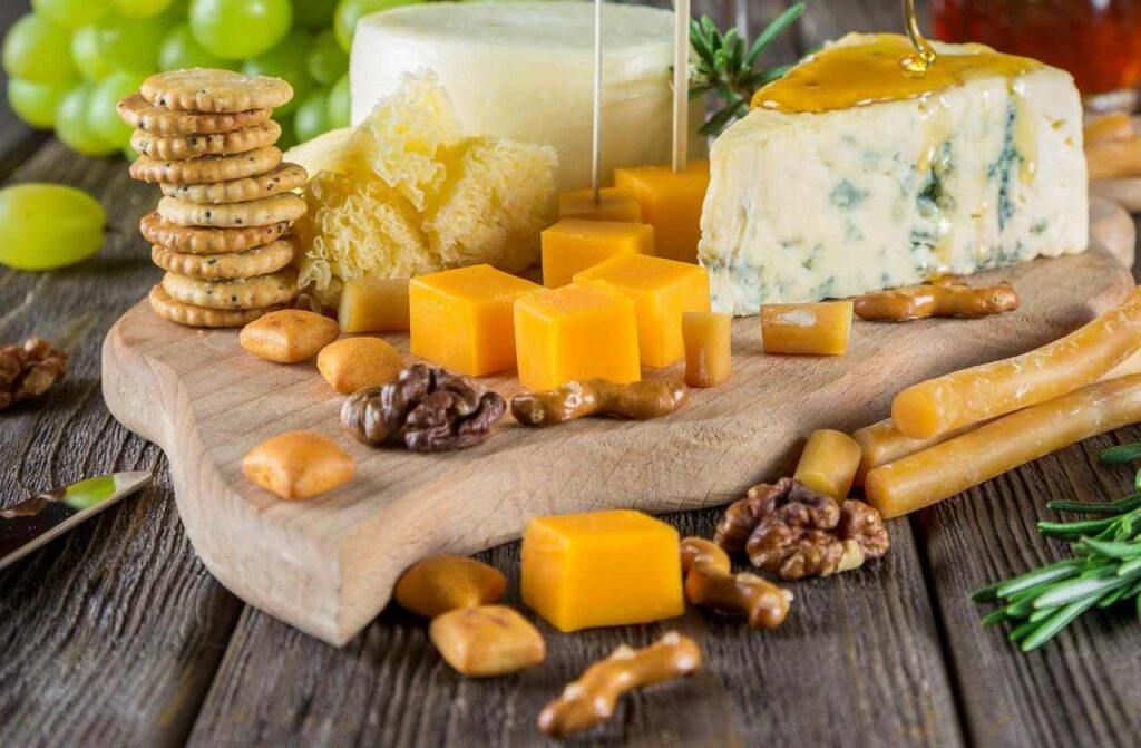 Cheese platter with assorted crackers, nuts, and honey on a wooden board.