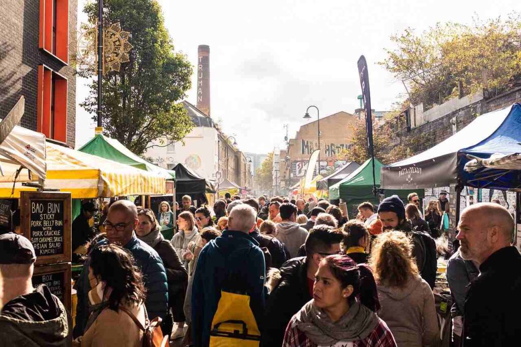 A crowded street market with numerous people browsing various stalls under colorful canopies, capturing the vibrant atmosphere of a busy urban market