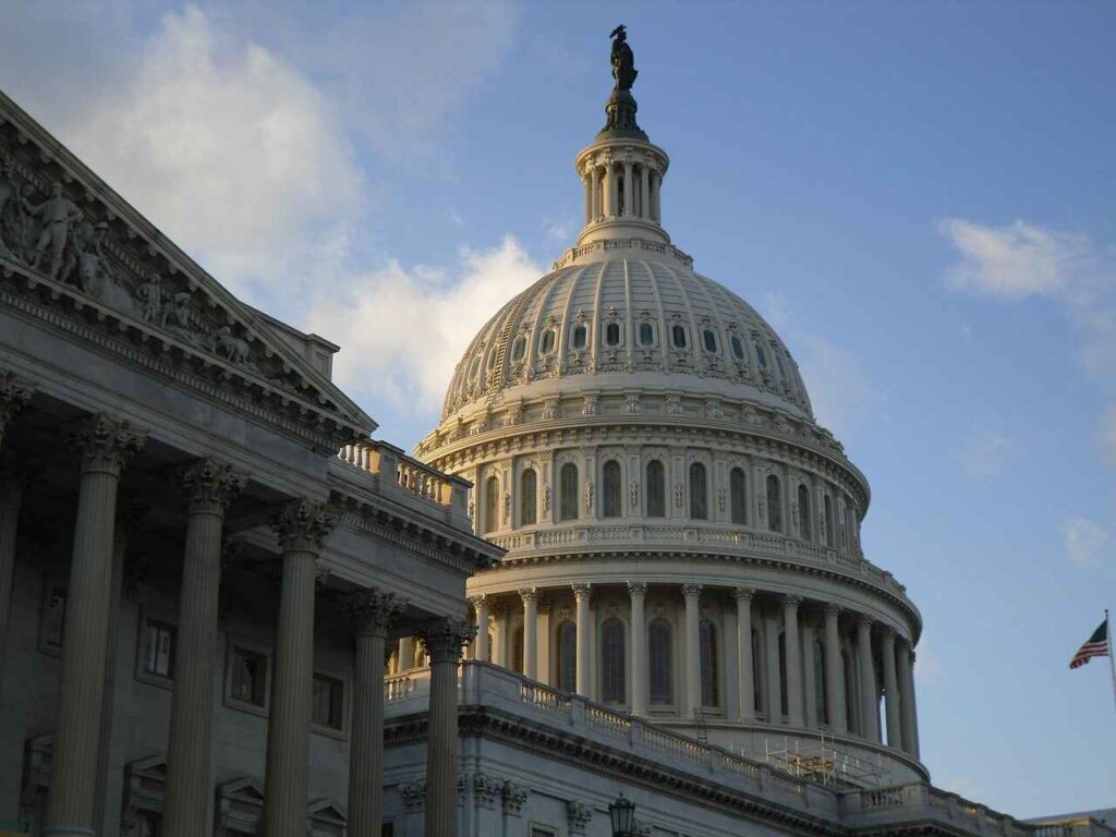 The dome of the United States Capitol building in Washington, D.C., bathed in soft sunlight with a clear blue sky in the background.